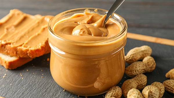 A whole jar of peanut butter, with a slice of bread on the left and whole peanuts on the right.