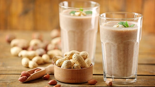 Two large glasses containing a peanut butter smoothie for bodybuilding.