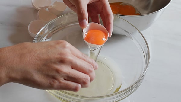 Une personne en train de casser un oeuf et de verser le blanc d'oeuf dans un saladier transparent.