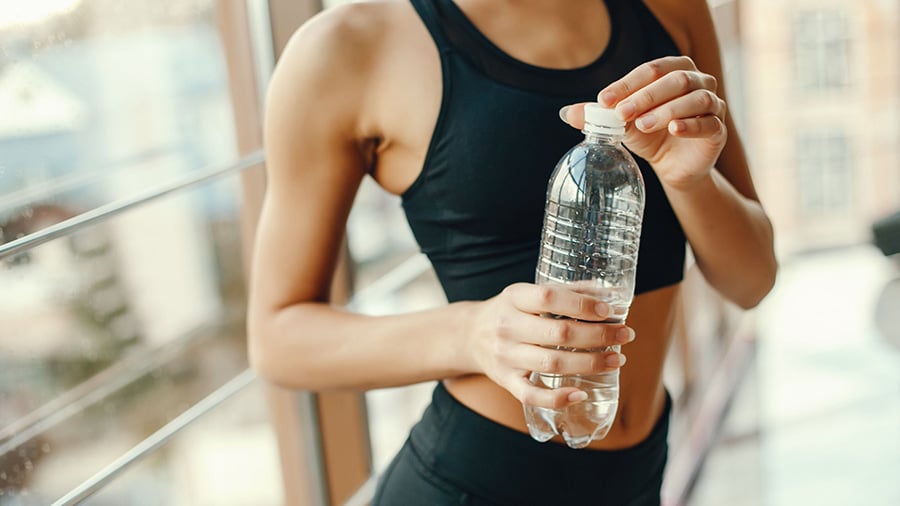 Une femme en tenue de sport noire, tenant une bouteille d'eau dans les mains.