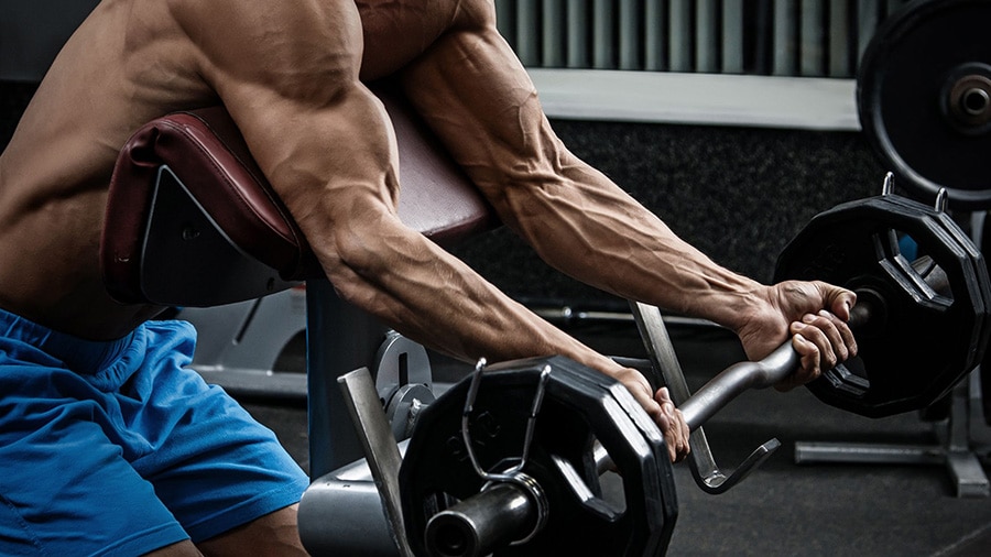 A man performs the larry scott curl biceps exercise in a weight room.