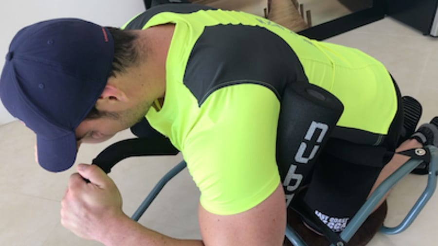 Le coach sportif Julien Quaglierini, portant un t-shirt jaune et une casquette, en train d'utiliser le Nubax pour soulager ses douleurs au dos.