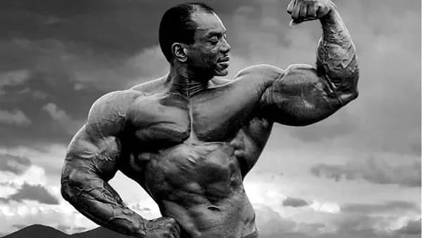 Shirtless bodybuilder Sergio Oliva in full biceps contraction.