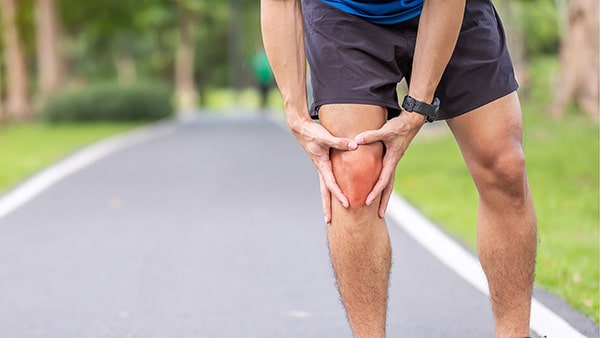 A runner stops his running session by holding his right knee with both hands.