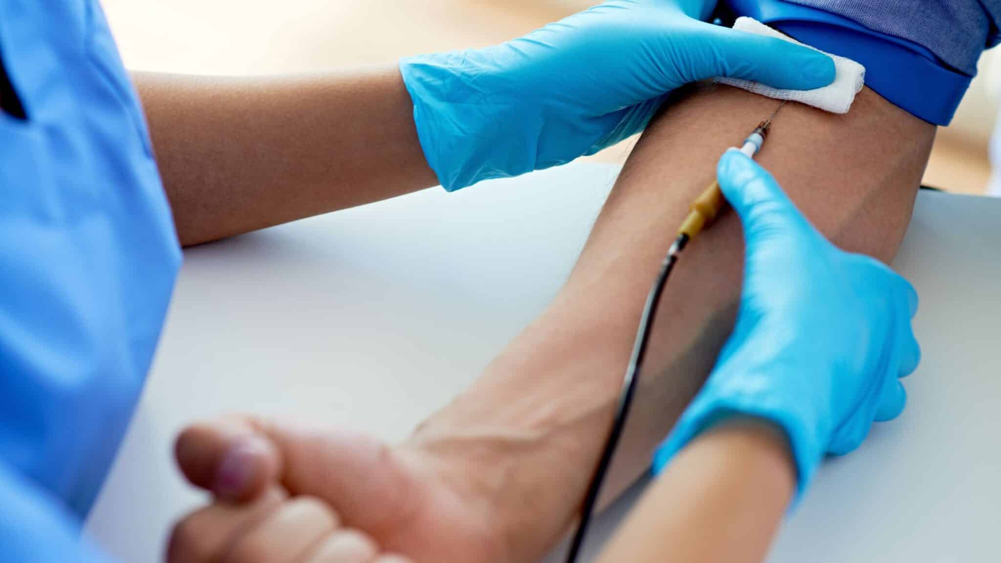 Un médecin muni de gants bleus réalise une prise de sang, piquant le pli du coude d'un patient avec une seringue.