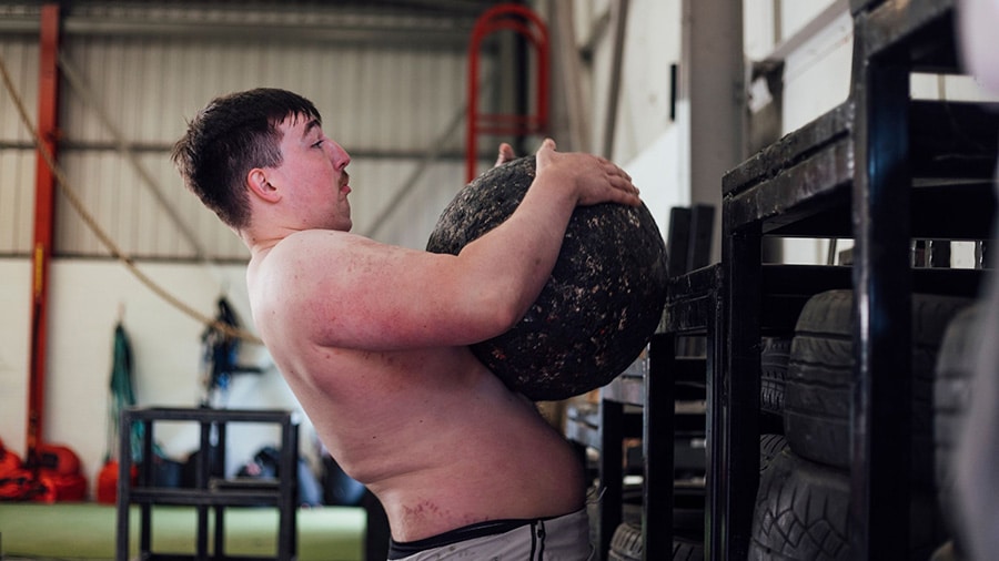 Un strongman torse nu soulève une pierre d'Atlas dans une salle de sport.