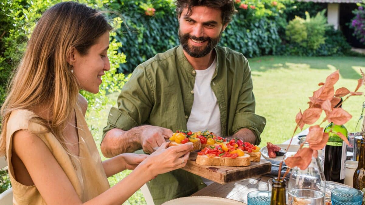 Un homme et une femme souriant dans un jardin, en train de manger un repas sain et équilibré.