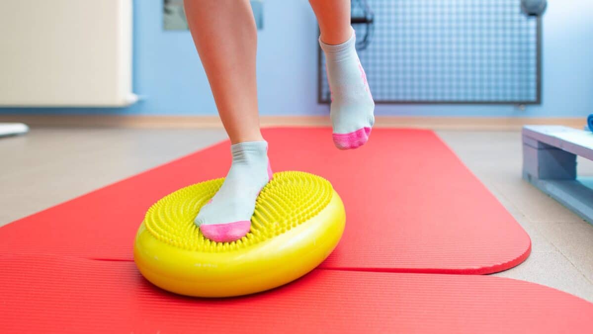 Une personne fait un exercice de proprioception sur un coussin d'équilibre posé sur un tapis de fitness.