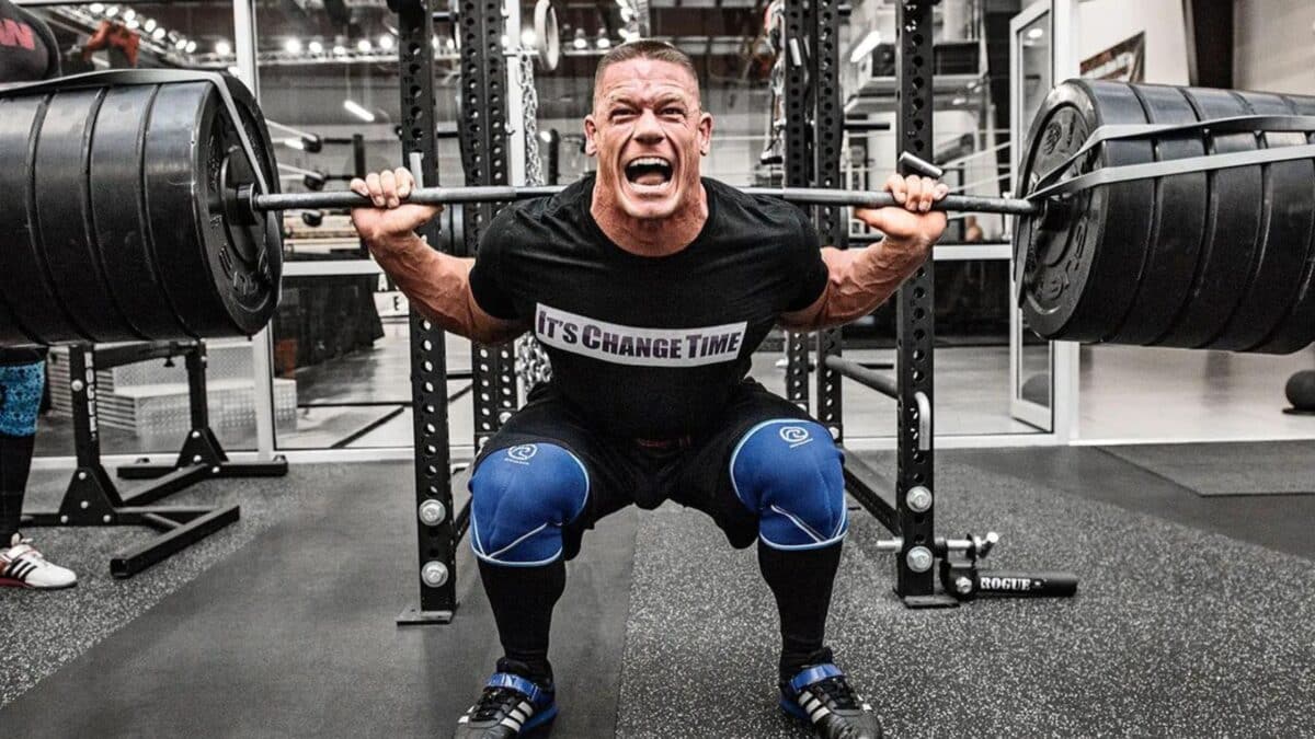 Wrestler John Cena doing squats in a weight room.