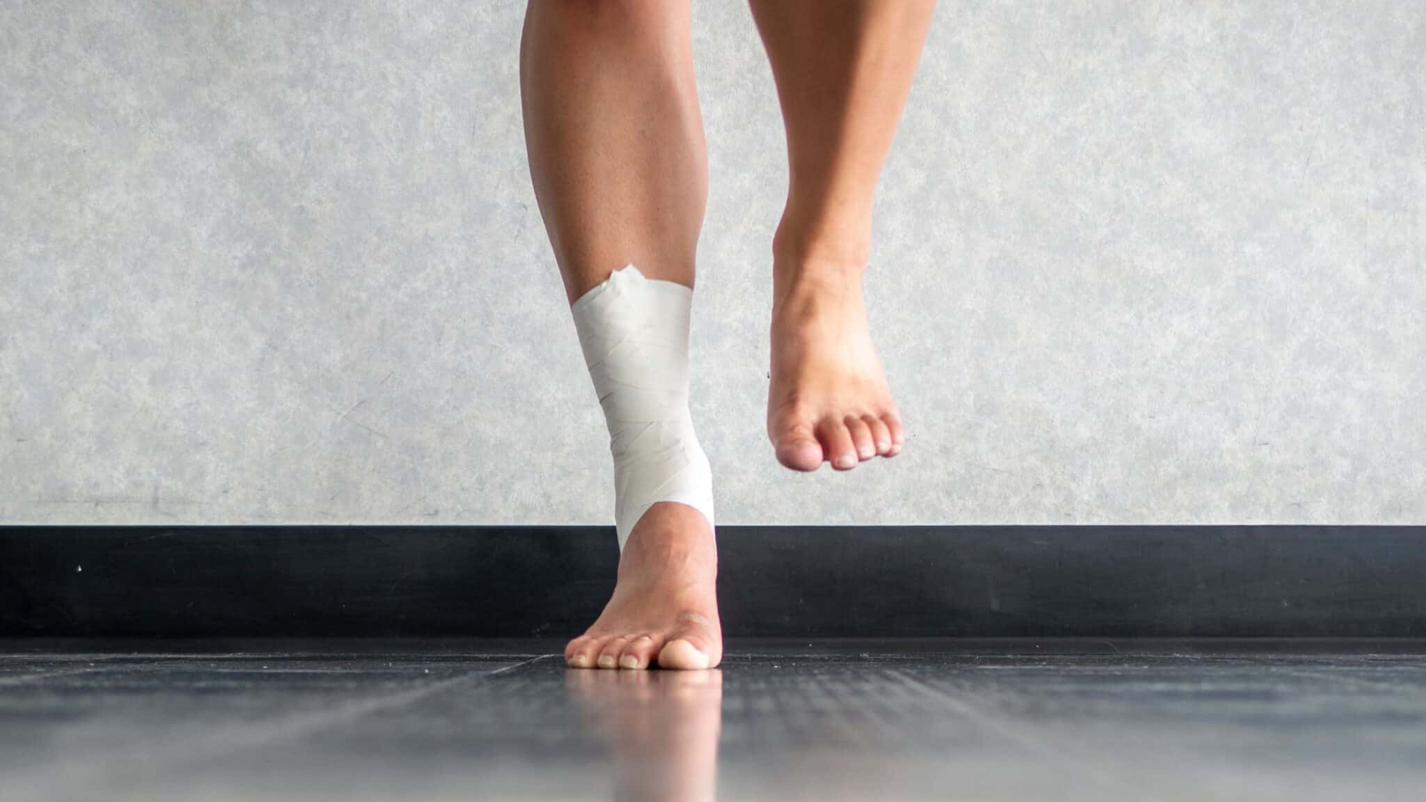 A person stands on his right leg, with his ankle bandaged as if he had suffered an injury.