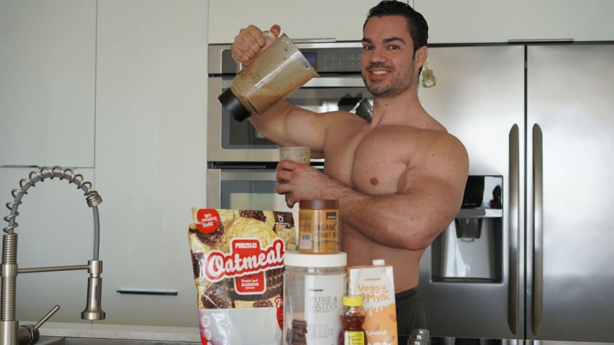 Le coach sportif Julien Quaglierini, torse nu, en train de préparer une recette de shaker pour la prise de masse avec du beurre de cacahuète.