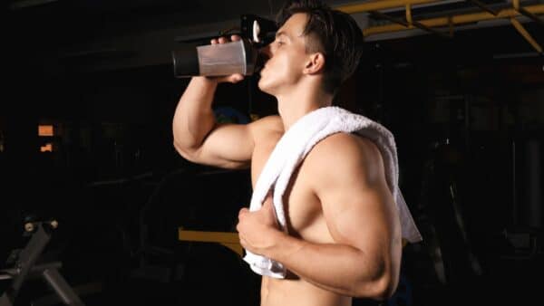 A shirtless man with a towel over his shoulder drinks a shaker with citrulline to enjoy its benefits.