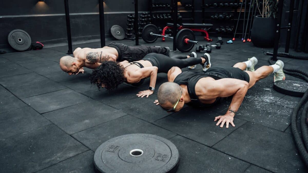 Two men and a woman do push-ups in a weight room.