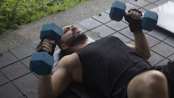 A man does a floor press with dumbbells, lying on the floor.