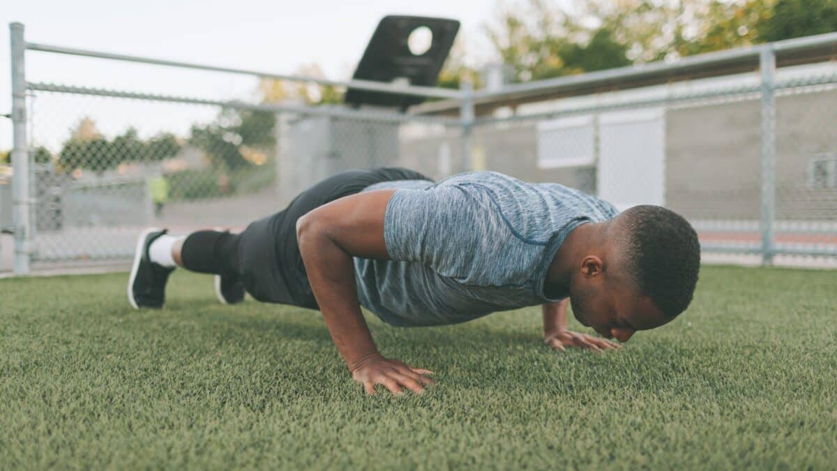 A man does push-ups outside on the grass.
