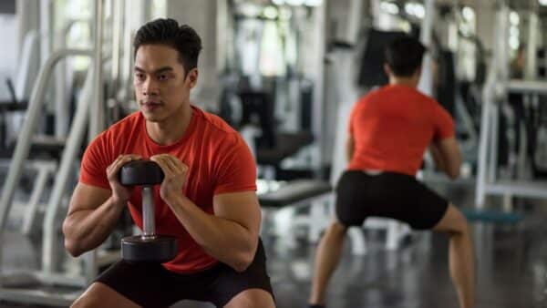A man does a goblet squat in a gym to strengthen his thighs.