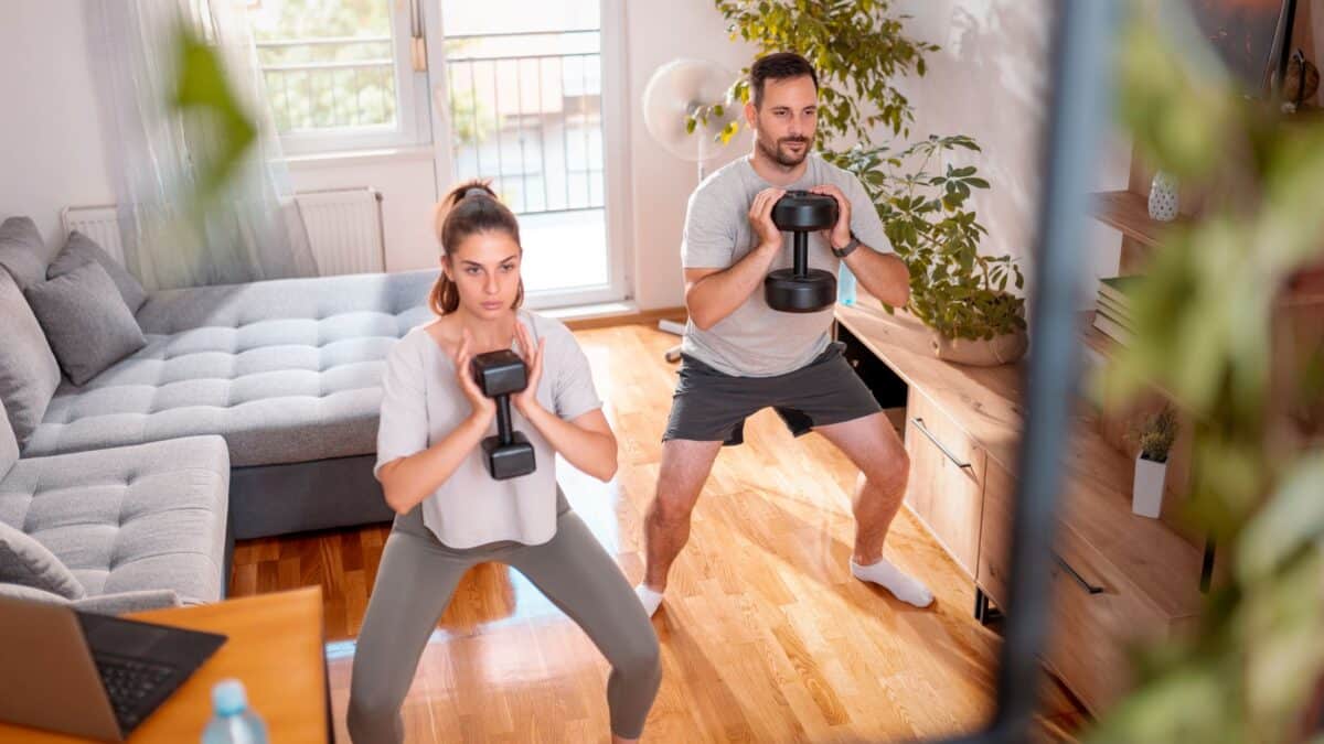 A man and a woman goblet squat in the living room of their apartment.