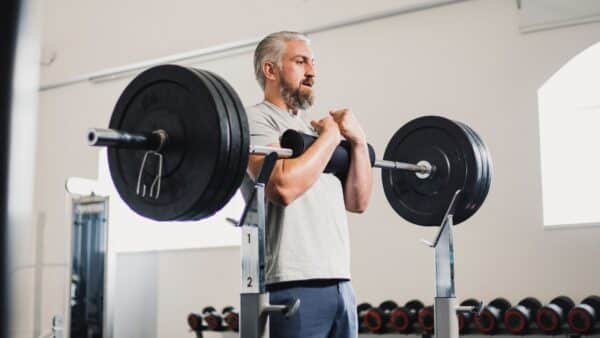 Un homme fait l'exercice du zercher squat dans une salle de musculation.