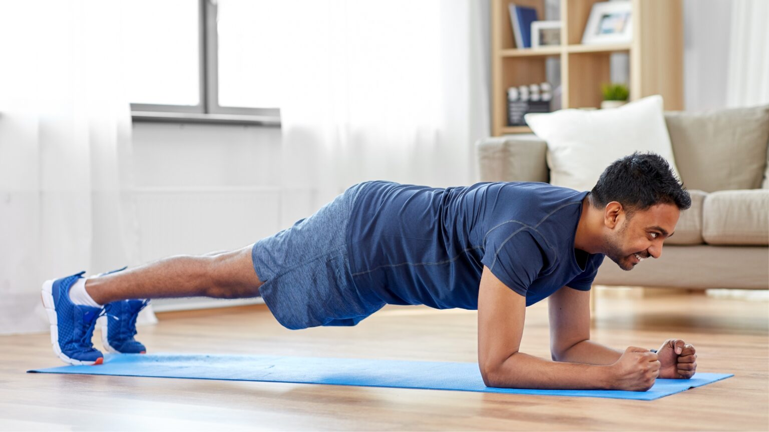 Un homme en tenue de sport effectue un exercice de gainage sur un tapis de fitness dans son salon.