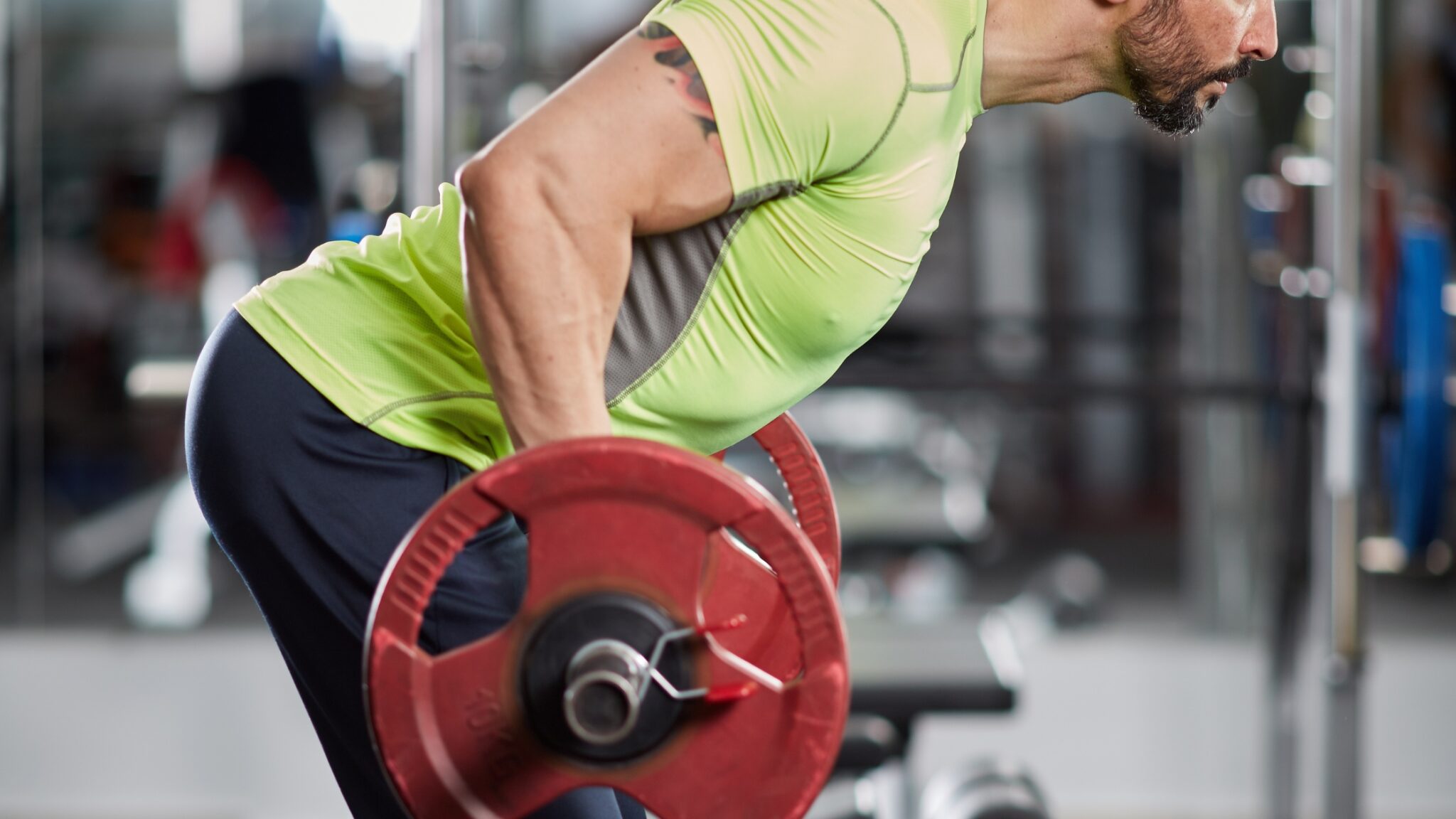 Un homme fait du rowing Yates avec une barre de musculation dans une salle de sport.