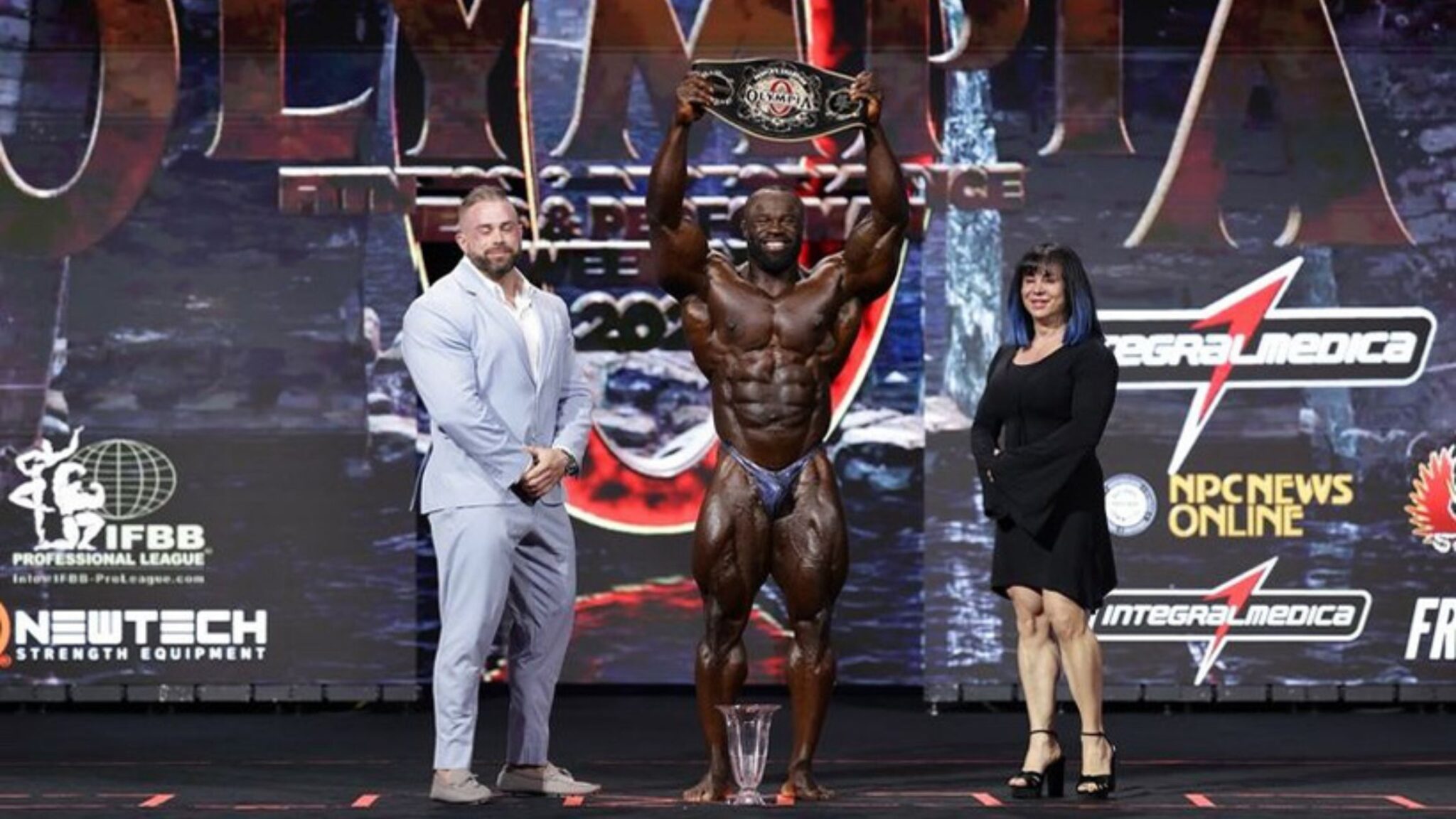 Le bodybuilder Samson Dauda, vainqueur de Mr Olympia 2024, soulève sur scène sa ceinture de champion.