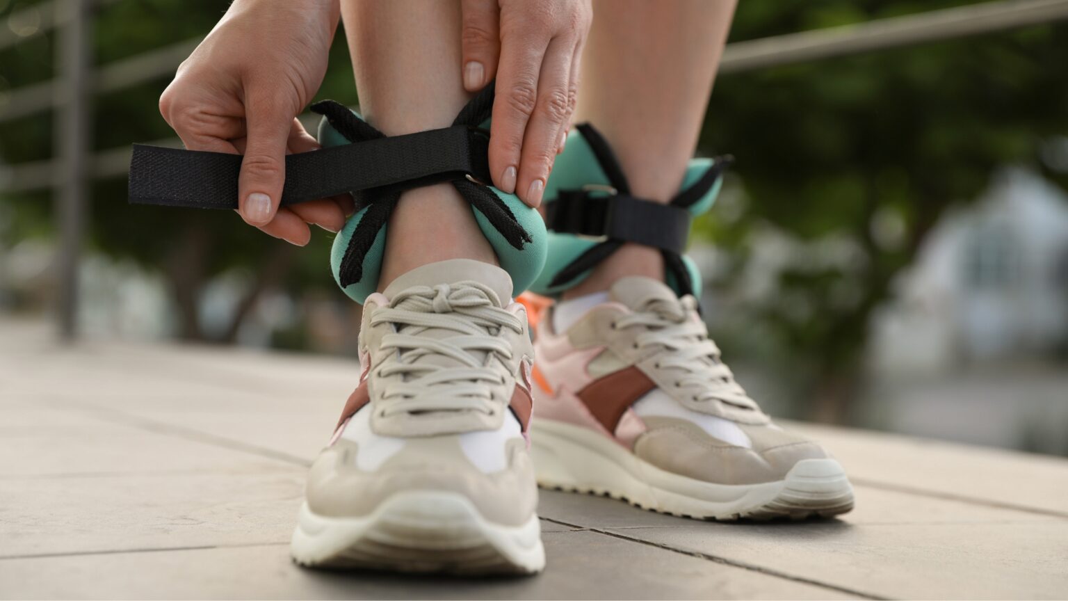 Une femme en chaussures de sport attache des poids de cheville vert et noir à ses chevilles.