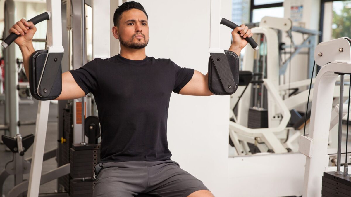 Un homme en tenue de sport fait du pec deck à la machine dans une salle de fitness.