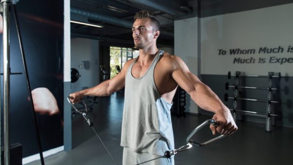 Un homme fait des élévations latérales à la poulie pour muscler ses épaule dans une salle de sport.