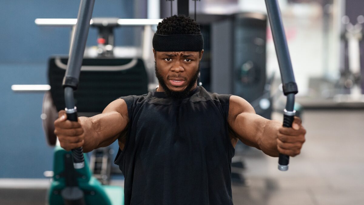 Un homme fait du pec deck, bras tendus vers l'avant, pour muscler ses pectoraux dans une salle de sport.