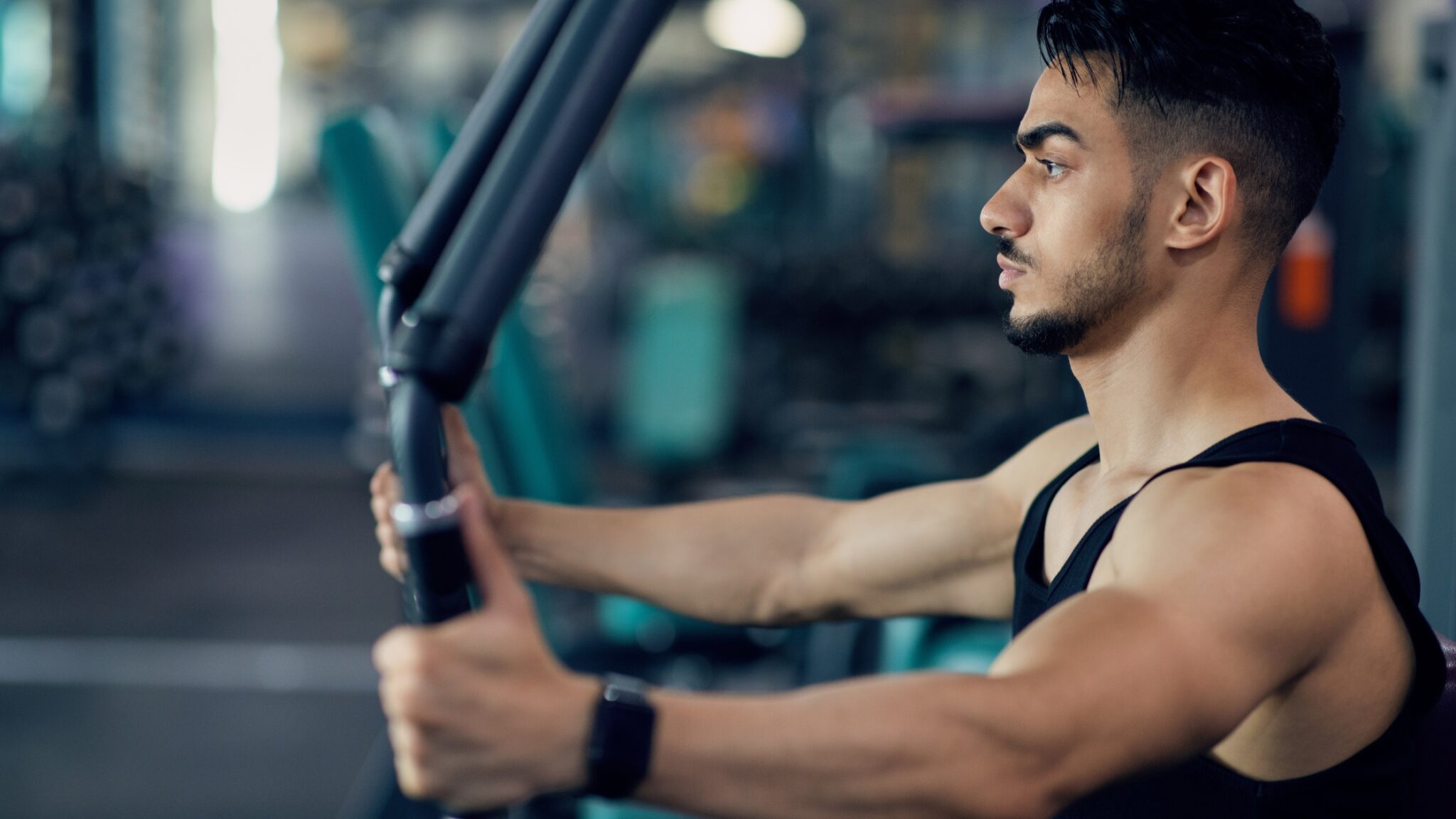 Un homme en débardeur travaille ses pectoraux au pec deck dans une salle de muscu.