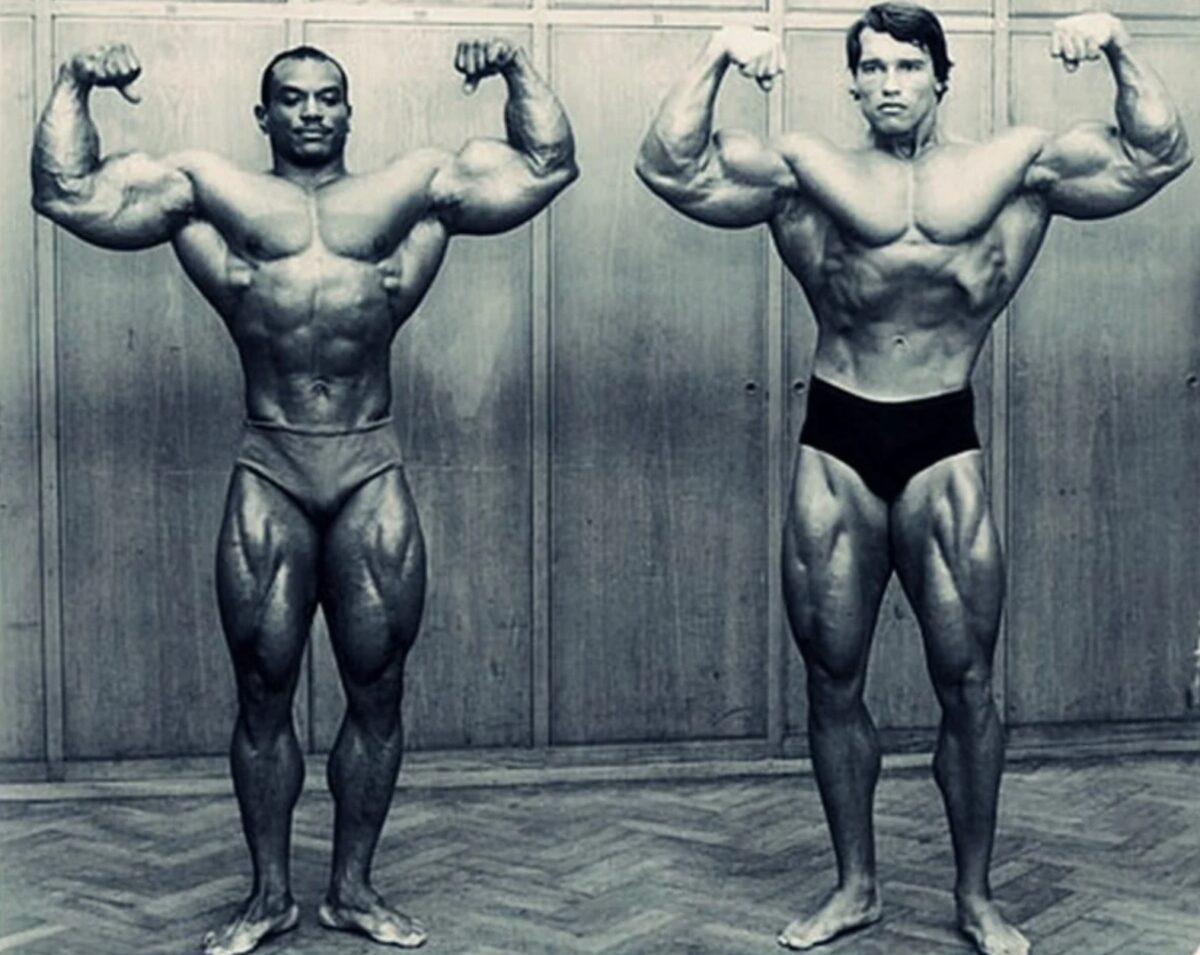 Les bodybuilders Sergio Oliva et Arnold Schwarzenegger, torse nu, côte à côte en train de contracter leurs biceps.