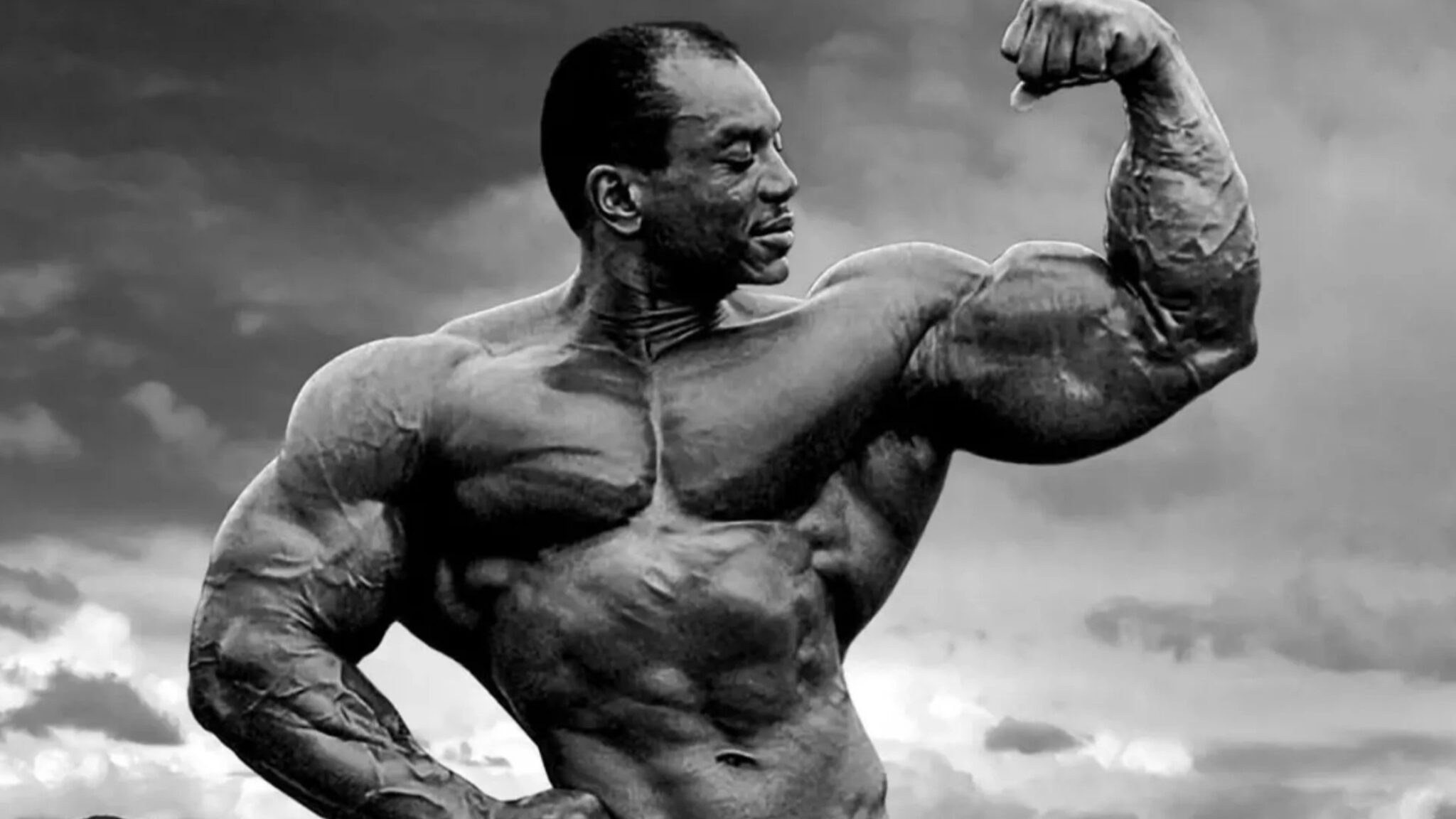 Le bodybuilder Sergio Oliva torse nu, contractant son biceps.