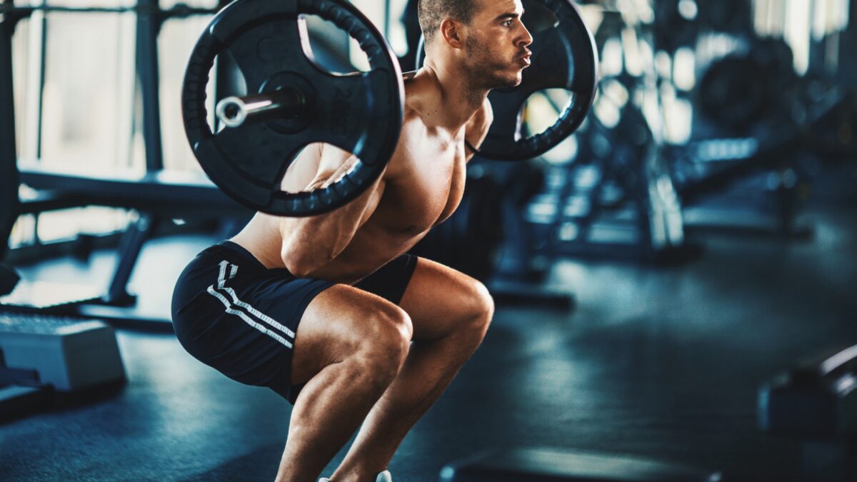 Un homme torse nu fait du squat dans une salle de musculation.