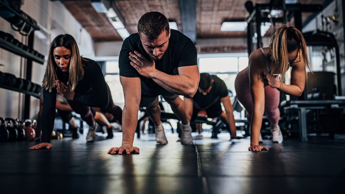 Des hommes et des femmes font du gainage dans une salle de sport.