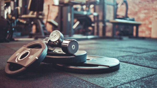 Des dalles installées dans une salle de sport, sur laquelle sont posés des disques de poids et des haltères.